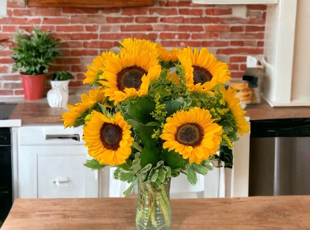 A SUNFLOWERS ARRANGEMENT on a wooden countertop with a brick wall in the background.