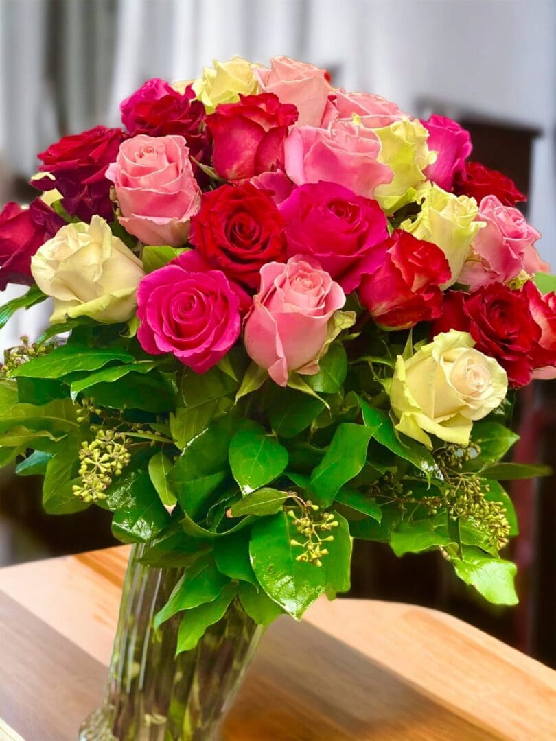 A vibrant bouquet of 50 Premium Assorted Long Stems Roses in clear vase arranged in a glass vase.