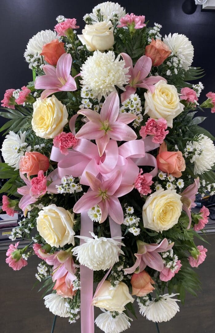 A stand with white and pink flowers and a pink ribbon