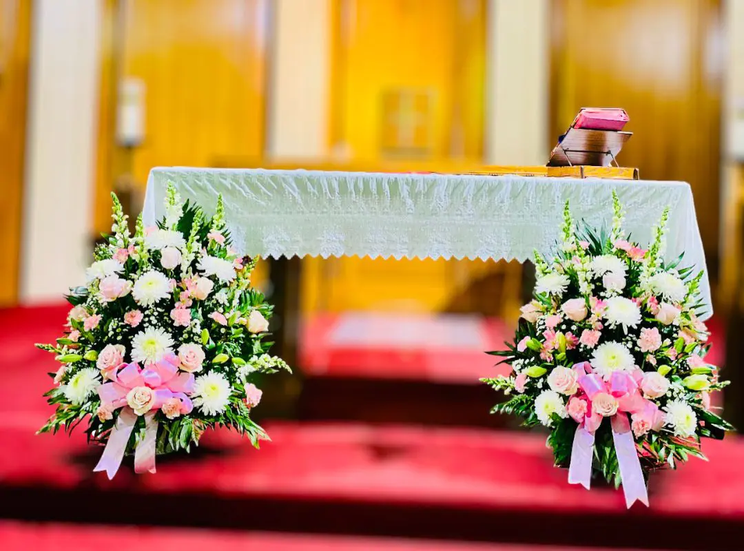 An altar adorned with two Premium 24 Red Roses Baskets and an open book, set against a backdrop of church doors.