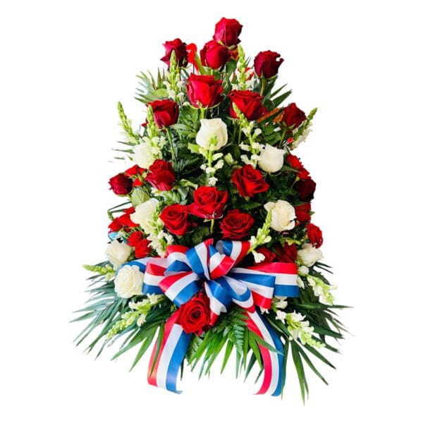 A floral arrangement featuring red and white roses with green foliage and a red, white, and blue ribbon.