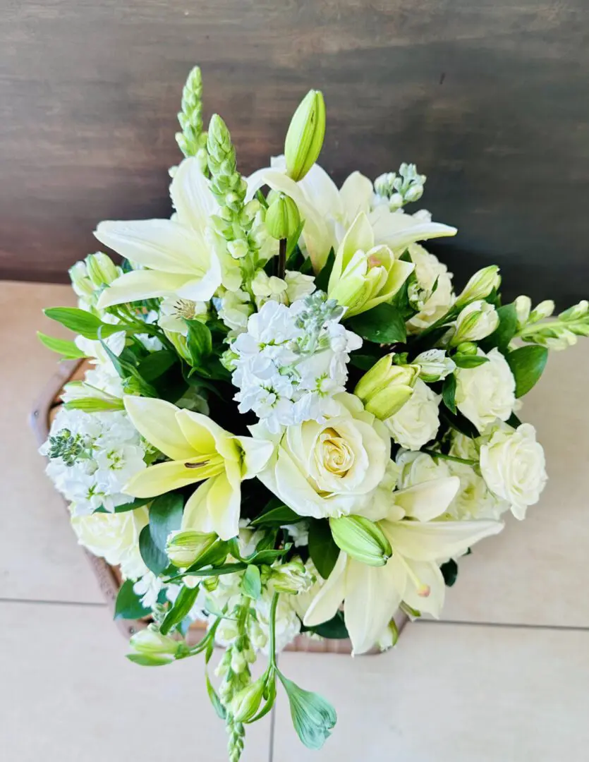 A fresh bouquet of white lilies, roses, and assorted complementary flowers positioned on a wooden surface.