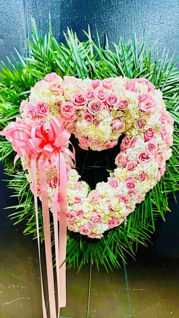 Funeral and Sympathy Open Heart White and Pink-shaped floral arrangement with pink and white roses and greenery, adorned with a pink ribbon.