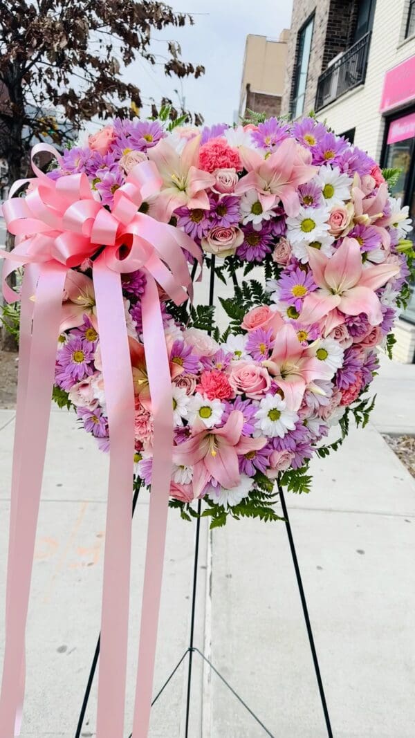 Floral wreath with pink and purple flowers and pink ribbons on a stand.
Product Name: Floral Open Heart Pink and White