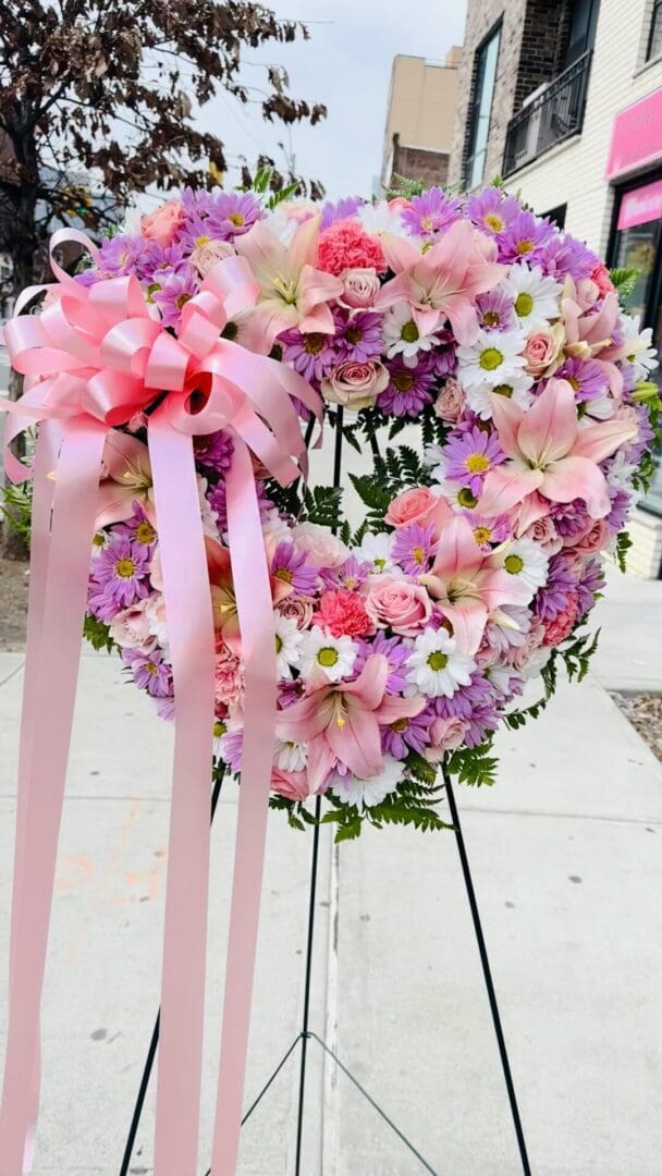 Floral wreath with pink and purple flowers and pink ribbons on a stand.
Product Name: Floral Open Heart Pink and White