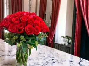 A bouquet of 12 PAYASITOS ROSES IN VASE on a marble countertop with elegant drapes in the background.