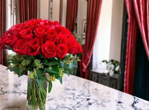 A bouquet of 12 PAYASITOS ROSES IN VASE on a marble countertop with elegant drapes in the background.