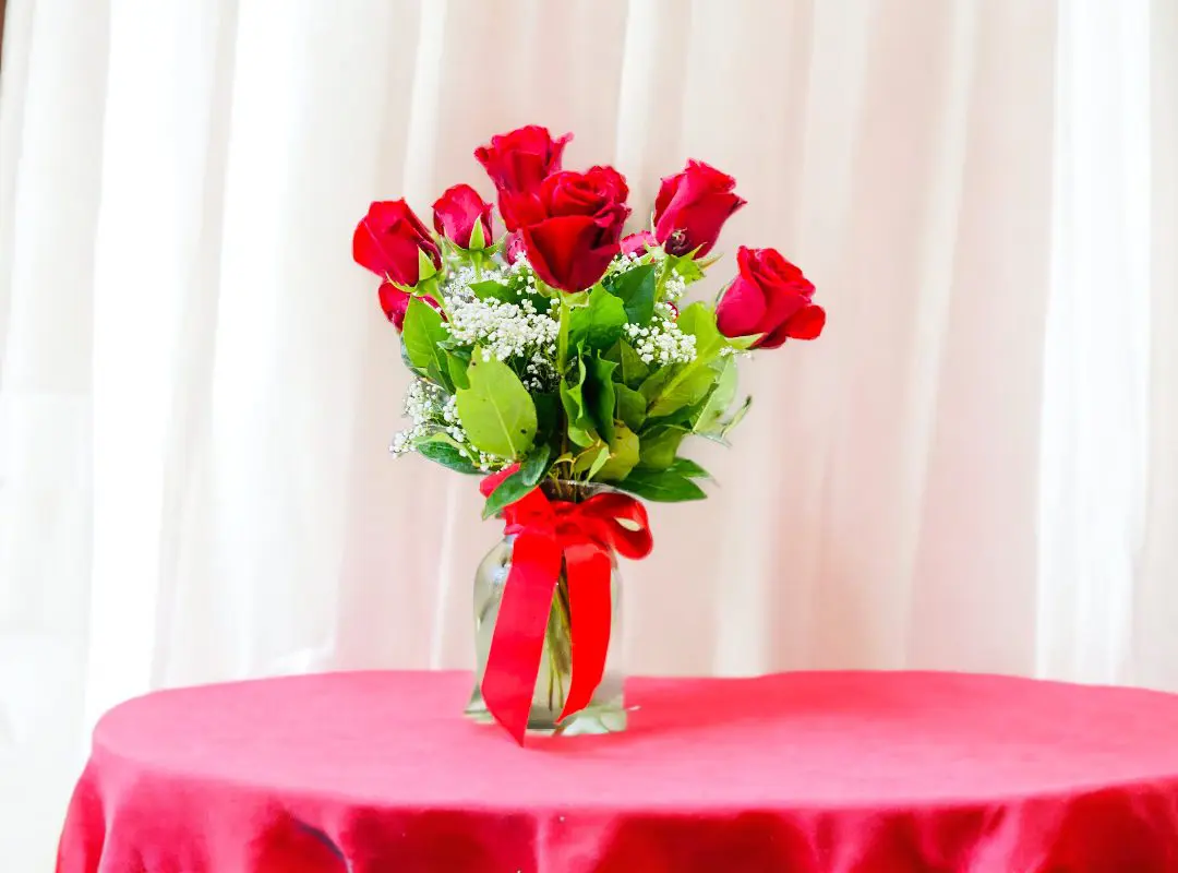 A bouquet of 12 PAYASITOS ROSES IN VASE with baby's breath on a red-covered table against a white curtain background.