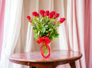 A bouquet of 12 PAYASITOS ROSES in a vase on a wooden table with a pink curtain backdrop.