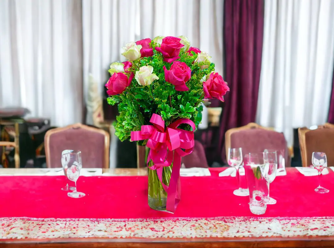 A vibrant bouquet of 12 PAYASITOS ROSES IN VASE on a red tablecloth in an elegant dining setup.