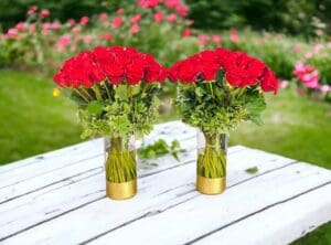 Two bouquets of 12 PAYASITOS ROSES IN VASE arranged in gold vases on a white wooden table with a garden in the background.