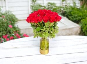 A bouquet of 12 PAYASITOS roses in a gold vase on a white wooden table with a blurred background.