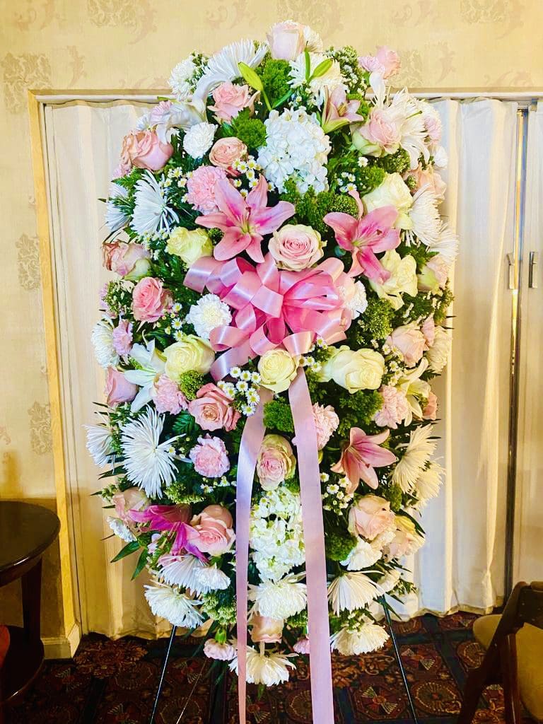 Large floral arrangement with pink and white flowers and ribbons displayed on a stand.