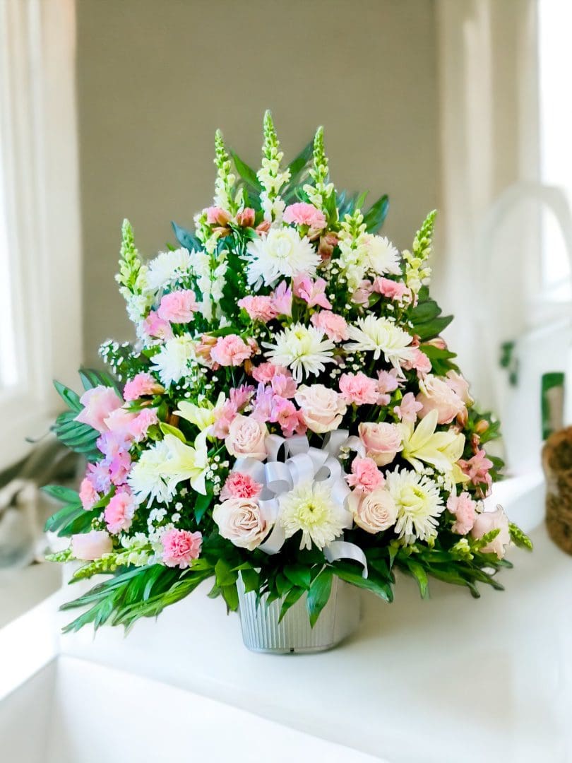 A vibrant bouquet of PINK AND WHITE SYMPATHY BASKET arranged in a vase atop a white surface.