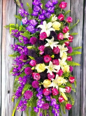 A vibrant floral arrangement featuring a mix of purple, pink, and yellow flowers with green fern accents.