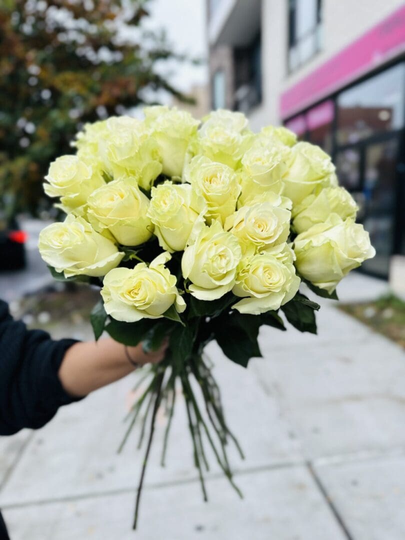 A person holding a bouquet of pale yellow roses.