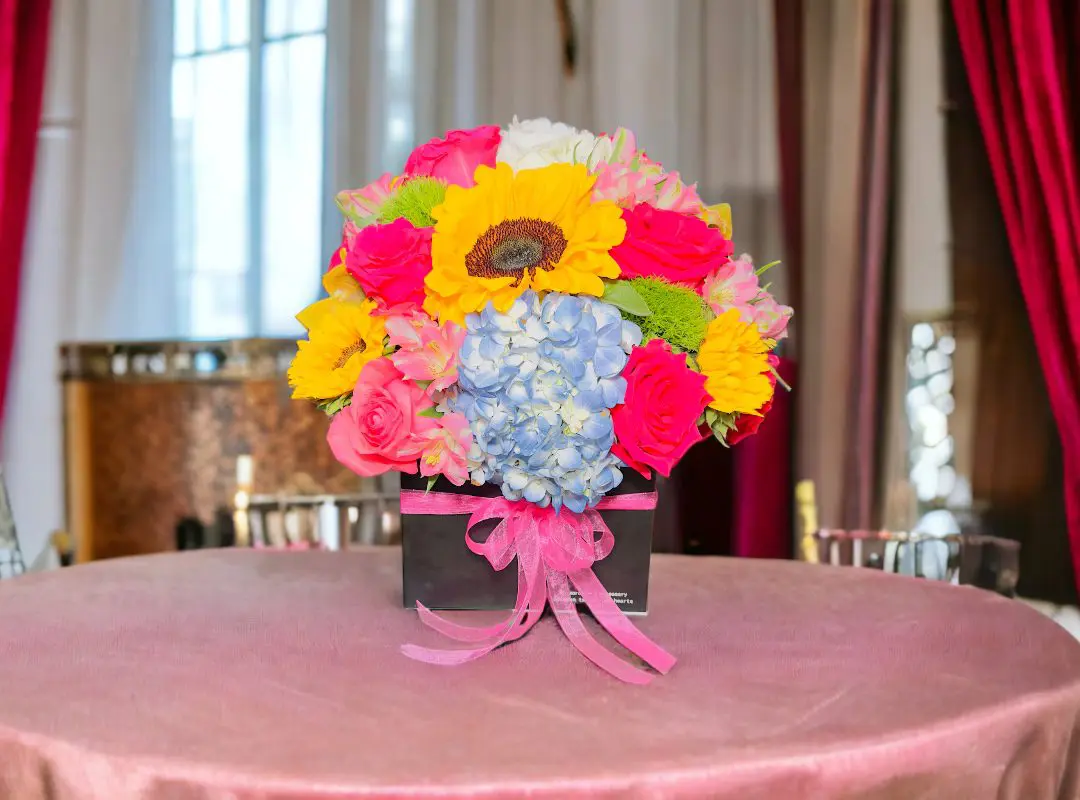 A vibrant bouquet of 12 Red Roses in Black Square Box on a table with a pink cloth.