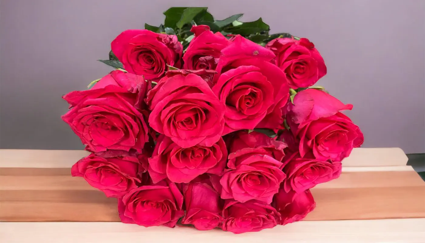 Bouquet of red roses on a wooden surface against a purple background.