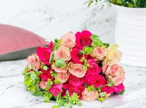 A vibrant bouquet of pink and cream roses on a marble surface with decorative elements in the background.