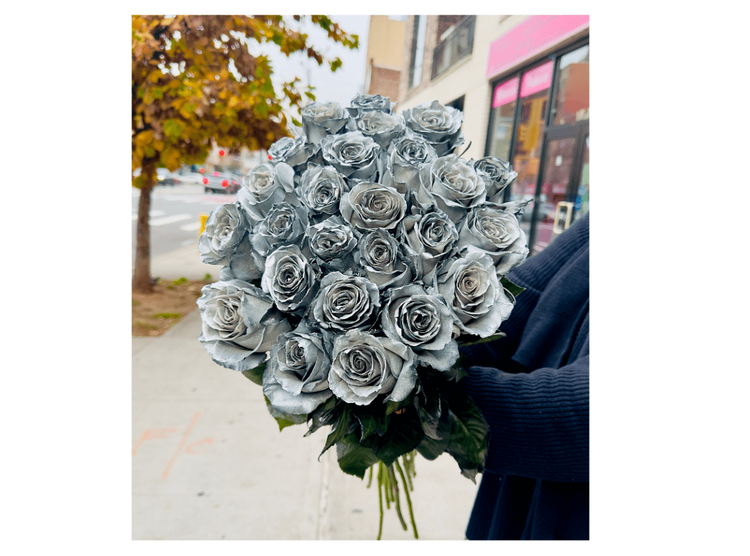 Person holding a large bouquet of silver-painted roses on a city street.