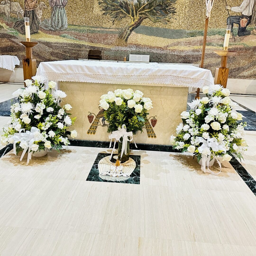 An altar adorned with white floral arrangements and candles in a church setting.