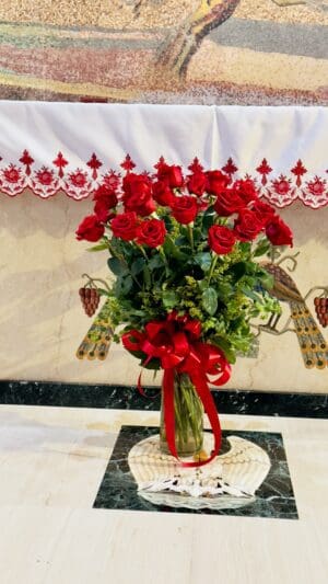 A bouquet of red roses arranged in a glass vase on a marble table, with a decorative mosaic backdrop.