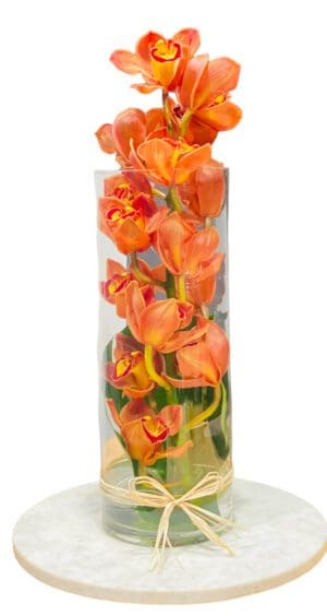 Orange flowers arranged in a tall glass vase on a marble base.
