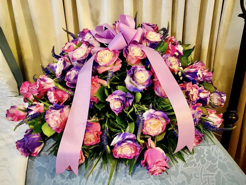 A bouquet of pink and purple roses with a satin ribbon on a table.