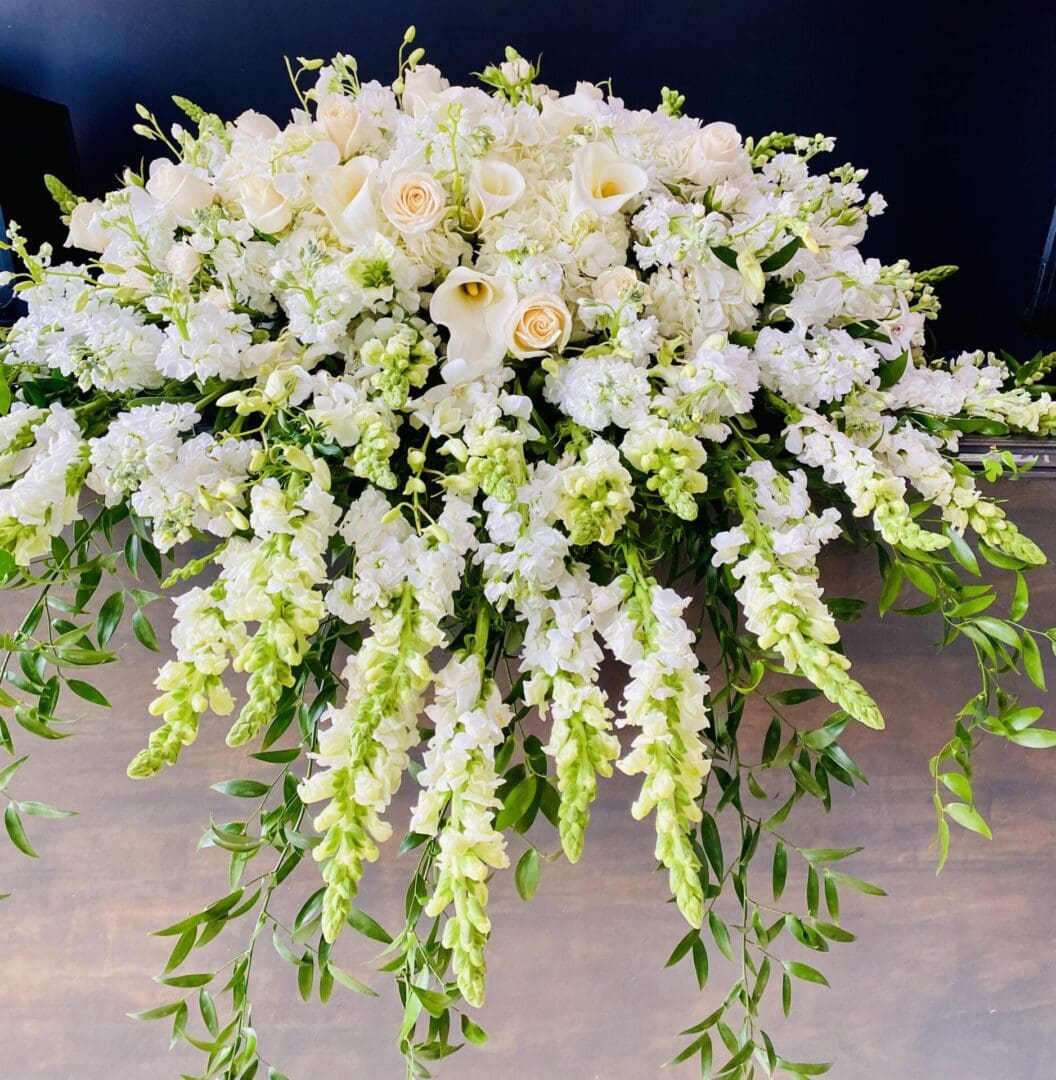 An elegant floral arrangement featuring white roses and cascading green foliage on a dark background.