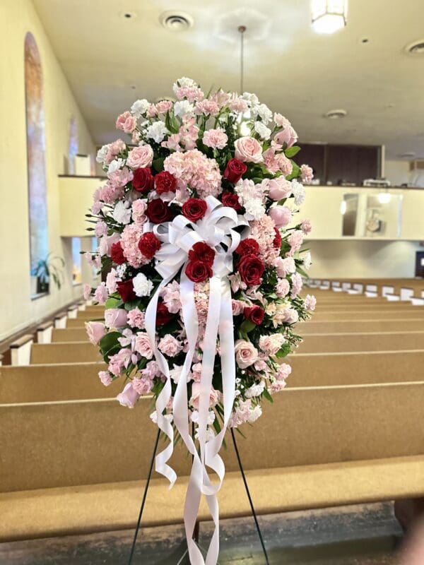 Floral arrangement with Red, Pink & White Standing Spray roses on a stand inside a church.