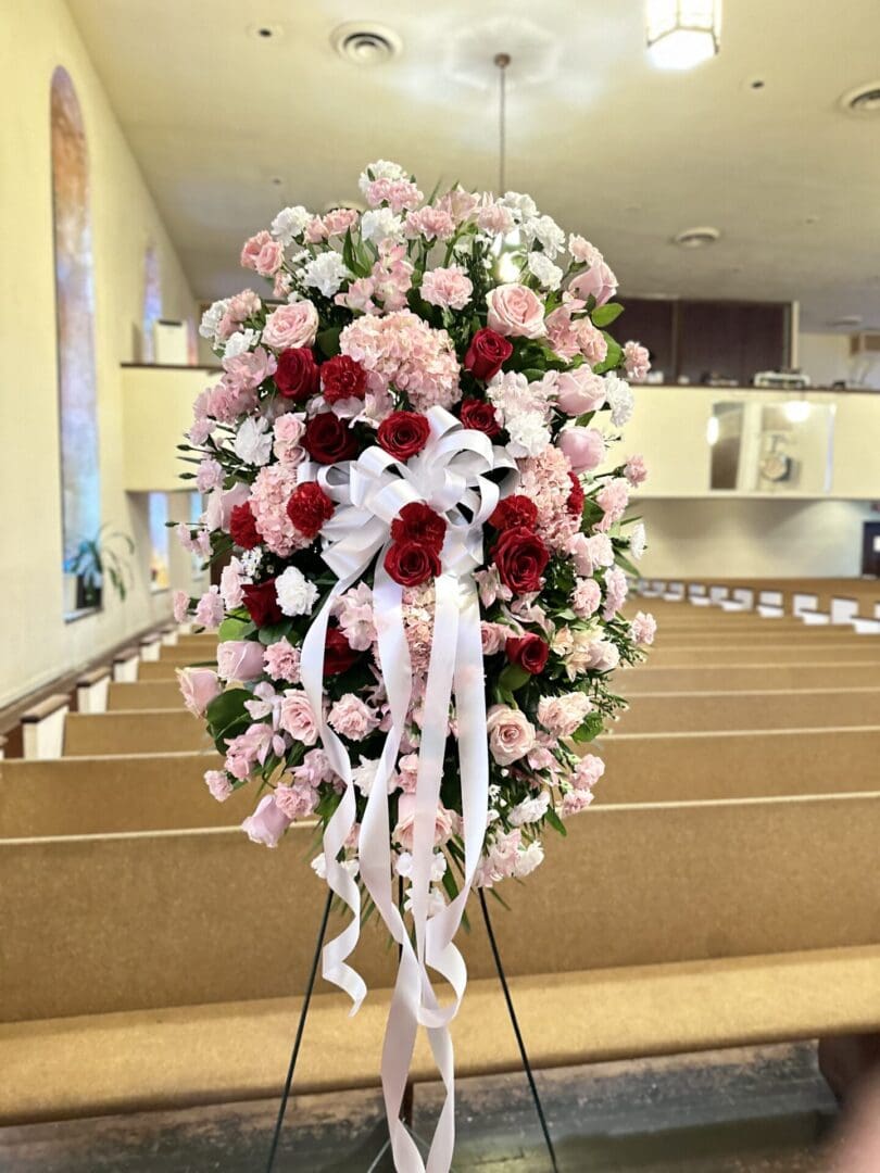 Floral arrangement with Red, Pink & White Standing Spray roses on a stand inside a church.